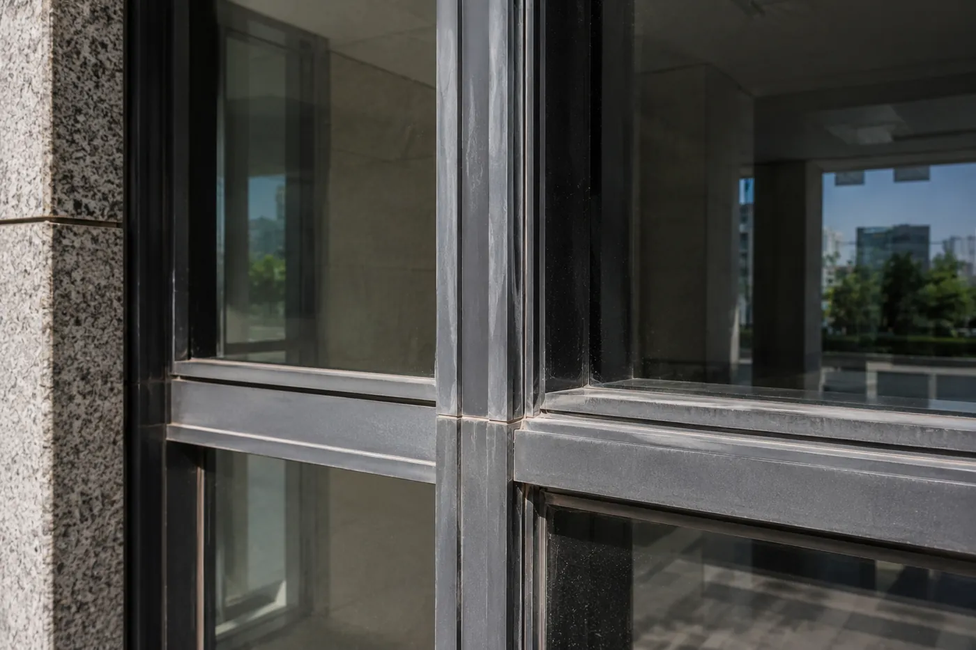 Aluminium curtain wall framing before the work — dulled, weathered profiles at the transom junction